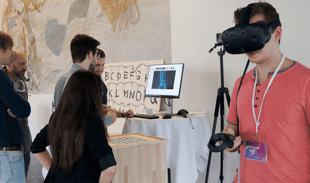 One person wears VR glasses, the other person stands in front of a screen